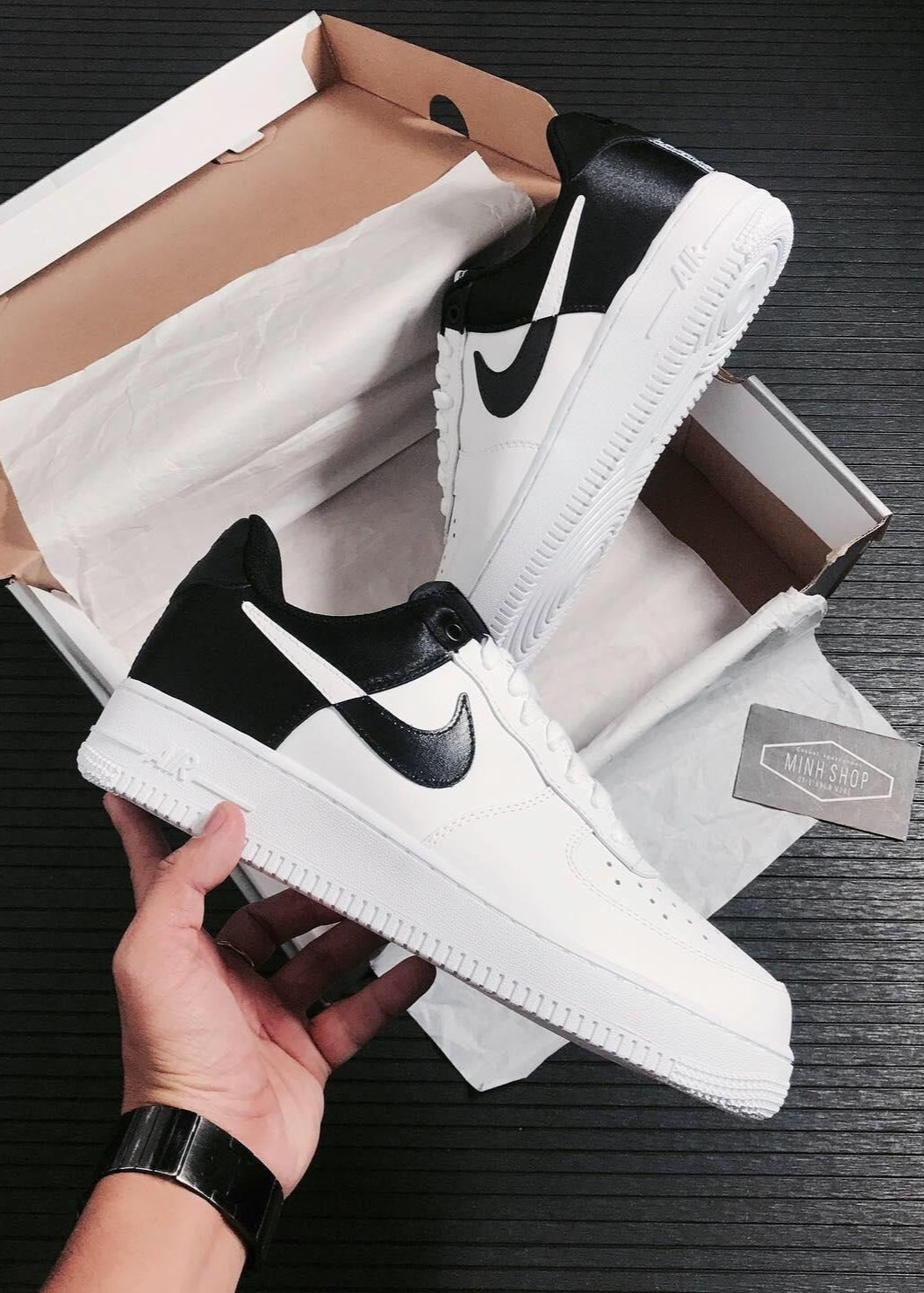 White and black sneakers with a Nike logo held above an open box on a dark surface.