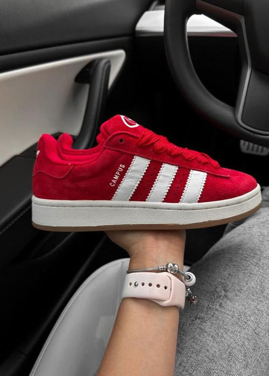 Red Adidas sneaker with white stripes worn inside a car.