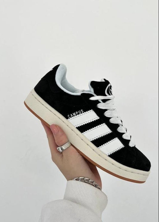 Black Adidas sneaker with white stripes held by a hand on a light gray background