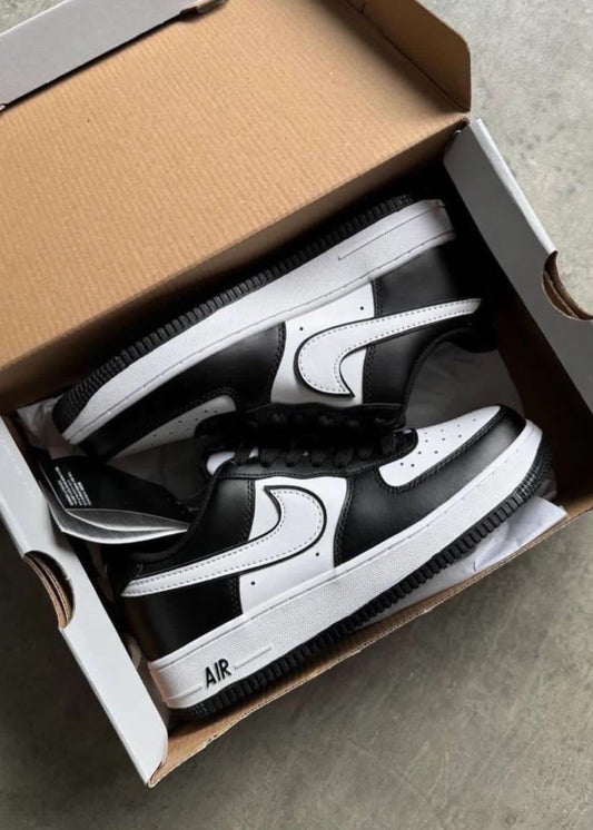 Black and white sneakers in an open cardboard box on a concrete floor.